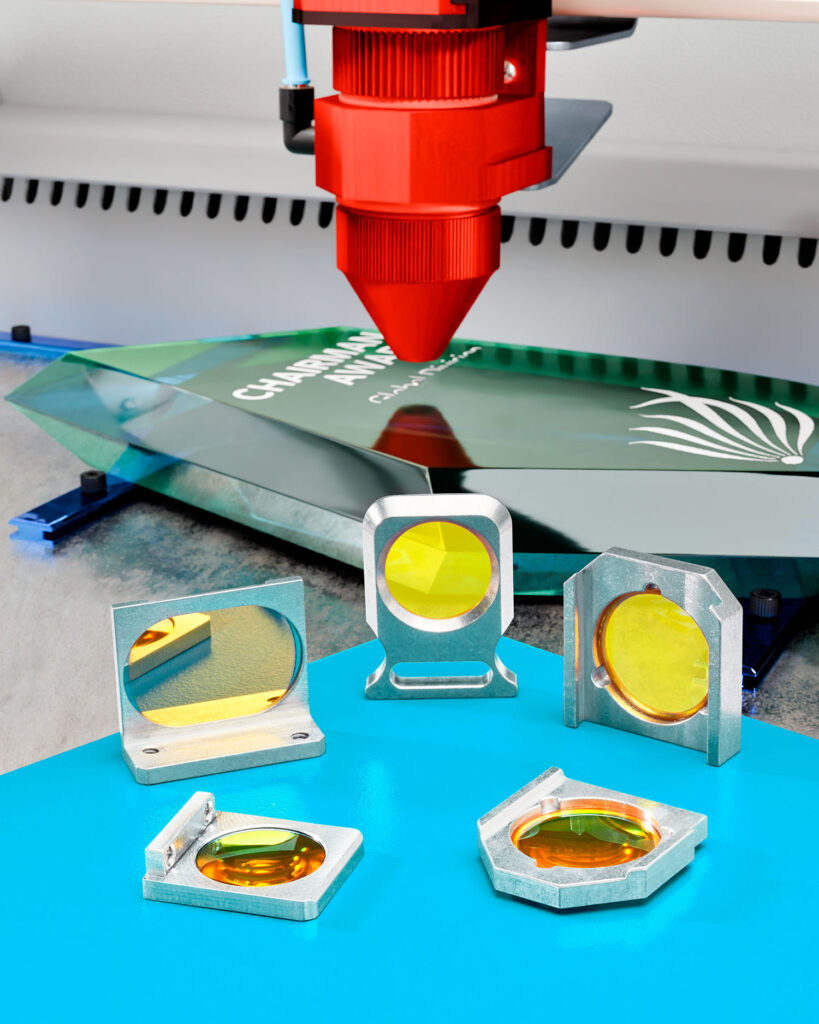 Mounted CO2 laser lenses sit on a blue table. A marking laser is working in the background