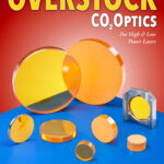 A variety of co2 laser lenses in different sizes and thicknesses are displayed on a blue table with the text "Overstock CO2 Optics" in bold at the top.