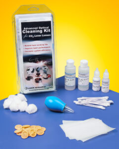 The packaging and contents of a laser optics cleaning kit sit on a blue table in front of a yellow background. Bottles of solution, wipes, cotton swabs, cotton balls and finger cots are spaced evenly.